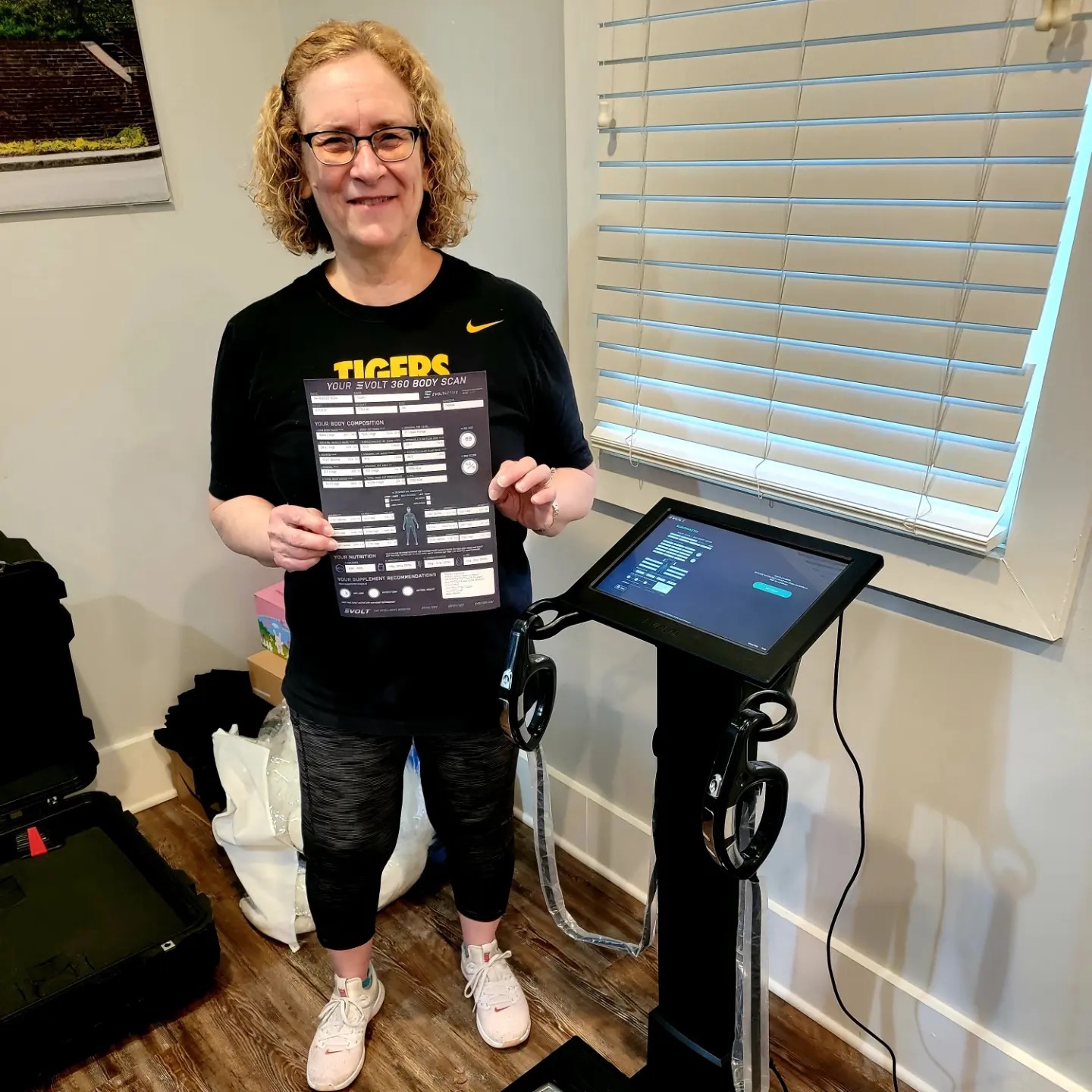 End Rezults Fitness female client holding her Evolt 360 body composition scan report beside the scanner